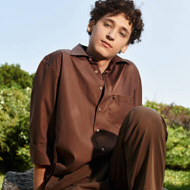 Curly haired young man relaxes in a vibrant park, embracing summer sunset