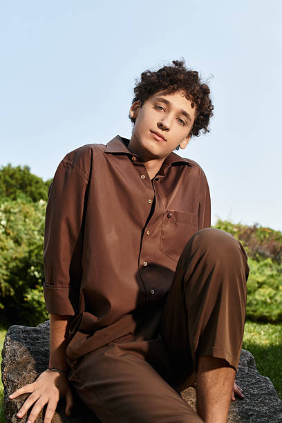 Curly haired young man relaxes in a vibrant park, embracing summer sunset